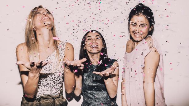 Drei junge Frauen feiern und werfen Konfetti in die Luft.