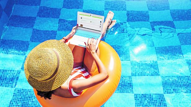 Woman in a swimsuit floating in inflatable circle in swimming pool and surfing the internet websites at her laptop pc. Leisure weekend and remote freelance work concept