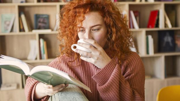 Woman sitting on sofa with mug of coffee in bookstore reading a book