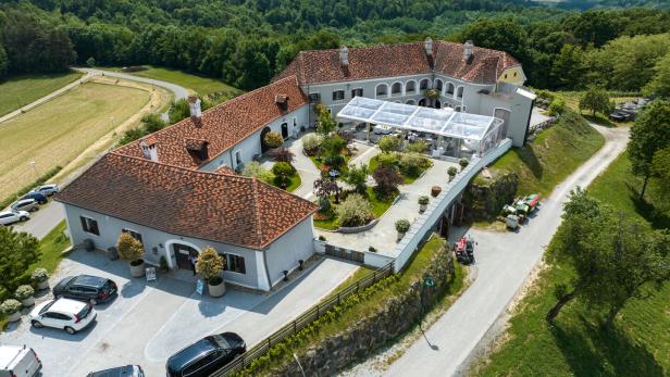 Luftaufnahme eines großen Gutshofs mit roten Dächern, Innenhof und Terrassen-Zelt, umgeben von grünen Hügeln.