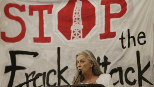 Eine Frau spricht vor einem Banner mit der Aufschrift „Stop the Frack“.