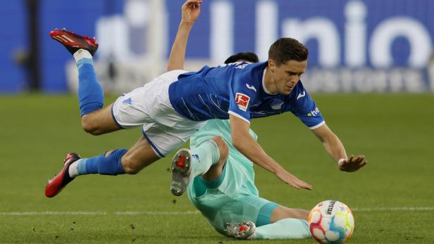 Ein Fußballspieler in blau-weißem Trikot stürzt über einen am Boden liegenden Torwart.