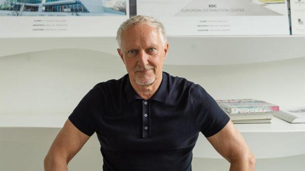 Dieter Brell, Gründer von 3deluxe, posiert vor einem Entwurf für ein EDC-Gebäude.