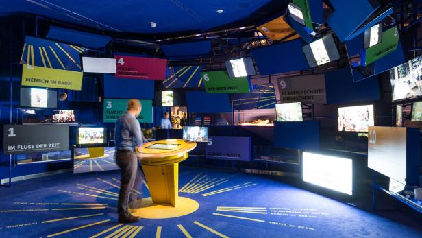 Ein Mann steht in einem Ausstellungsraum mit interaktiven Installationen und Bildschirmen.