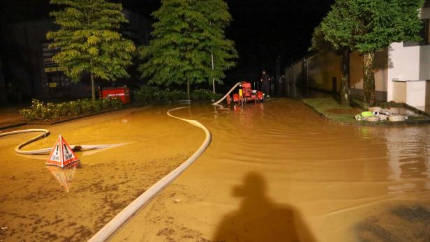 Ein überflutete Straße mit einem Feuerwehrmann und einer Pumpe bei Nacht.
