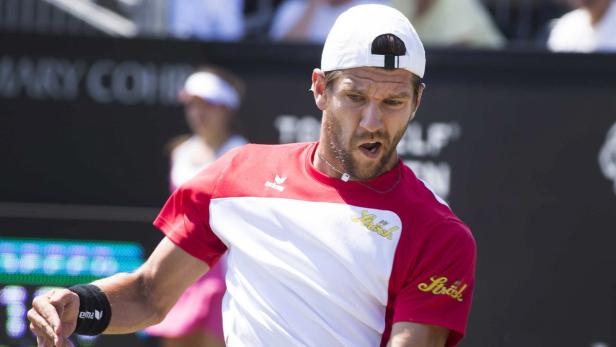 Ein Tennisspieler mit weißer Kappe und rotem Trikot auf dem Platz.