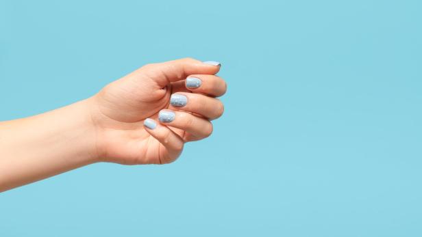 Eine Hand mit hellblau lackierten Fingernägeln vor einem hellblauen Hintergrund.
