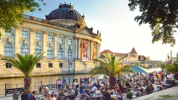 Auf der Museumsinsel in Berlin sitzen Menschen in einem Café am Ufer.