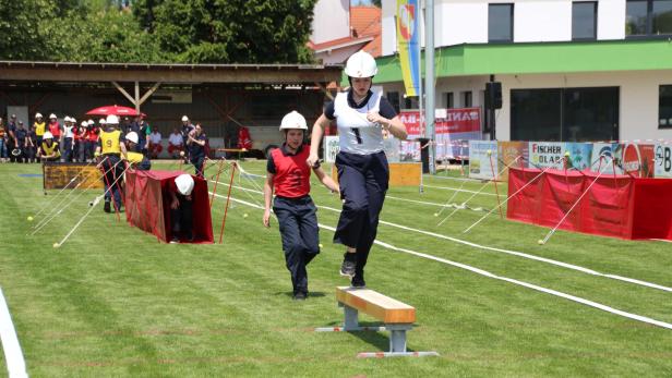 Zwei Jugendliche in Feuerwehrkleidung absolvieren einen Hindernisparcours auf einer Wiese.