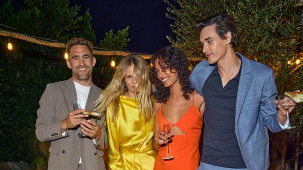 Vier Personen posieren mit Getränken und Pizza auf einer Holzterrasse.