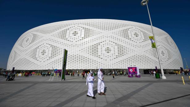 Zwei Männer in traditioneller Kleidung gehen vor dem Al-Thumama-Stadion in Katar entlang.