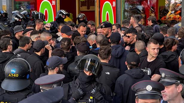 Eine Menschenmenge steht vor einem Geschäft für Thai-Massagen, bewacht von Polizisten.