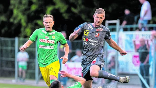 Ein Fußballspieler springt über einen am Boden liegenden Spieler, während ein dritter anläuft.