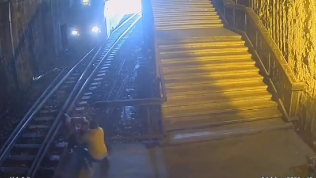 Zwei Personen befinden sich im Gleisbett, während sich ein Zug nähert.