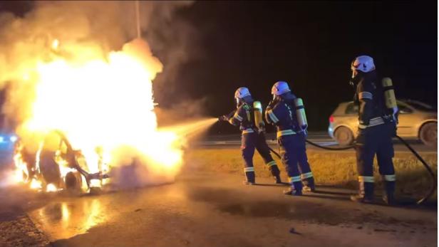 Feuerwehrleute löschen ein brennendes Fahrzeug auf einer Straße.