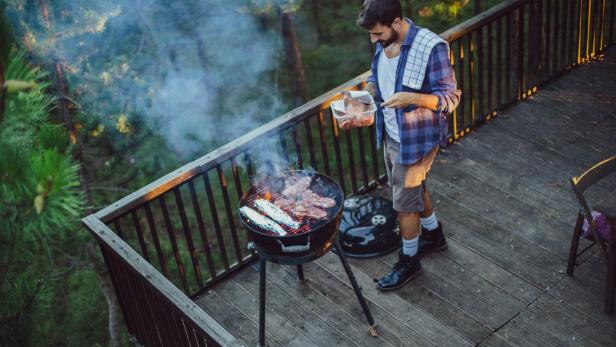 Ein Mann grillt Fleisch und Maiskolben auf einem Balkon.