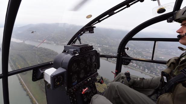 Ein Pilot im Cockpit eines Hubschraubers, mit einem anderen Hubschrauber in der Ferne.