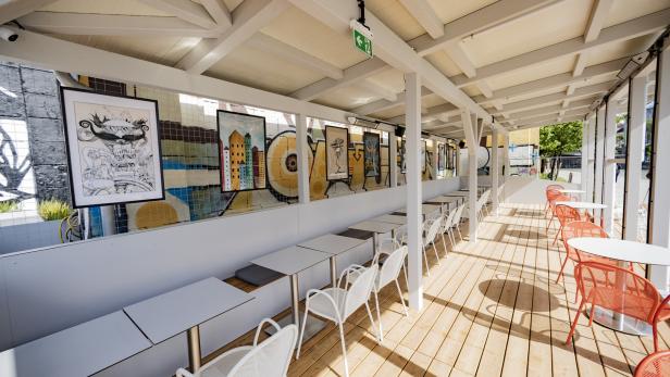 Ein Außenbereich eines Cafés mit Tischen, Stühlen und Kunstwerken an der Wand.