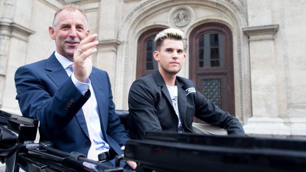 Ein Mann im Anzug und Dominic Thiem sitzen in einer Kutsche vor einem Gebäude.