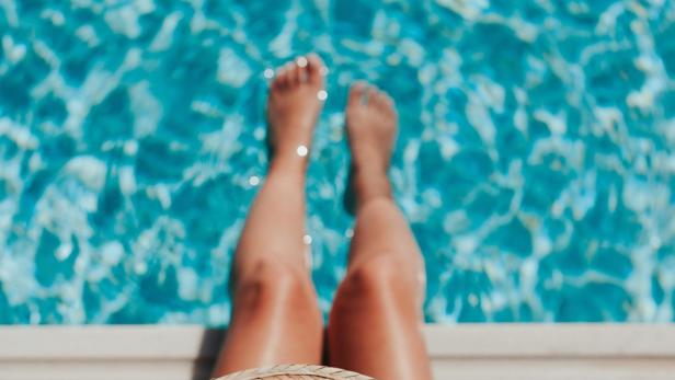 Eine Frau entspannt mit einem Strohhut am Pool.