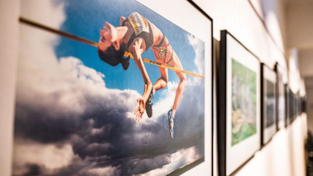 Ein gerahmtes Foto zeigt eine Hochspringerin vor blauem Himmel mit Wolken.