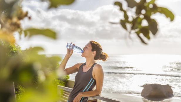 Eine Frau trinkt Wasser vor dem Hintergrund eines Strandes.