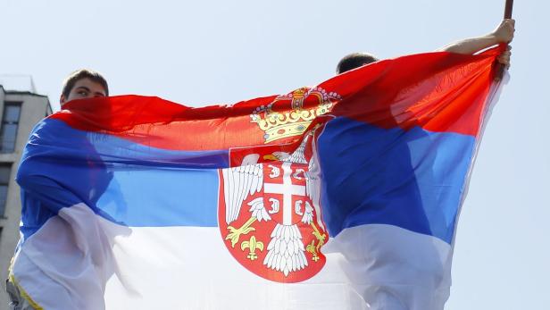 Zwei Personen halten eine serbische Flagge hoch.