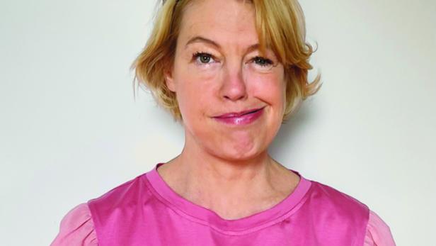 Eine Frau mit blonden Haaren und Sonnenbrille auf dem Kopf zwinkert in die Kamera.