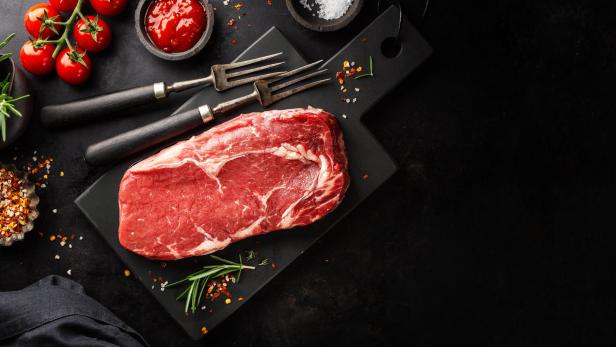 Ein rohes Ribeye-Steak liegt auf einem schwarzen Schneidebrett.
