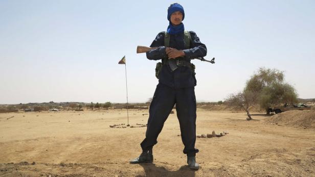 Ein Soldat in Uniform und Turban steht mit einem Gewehr in einer Wüstenlandschaft.