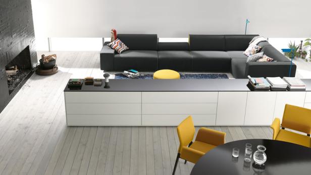Ein modernes Wohnzimmer mit schwarzem Sofa, weißer Kommode und gelben Akzenten.