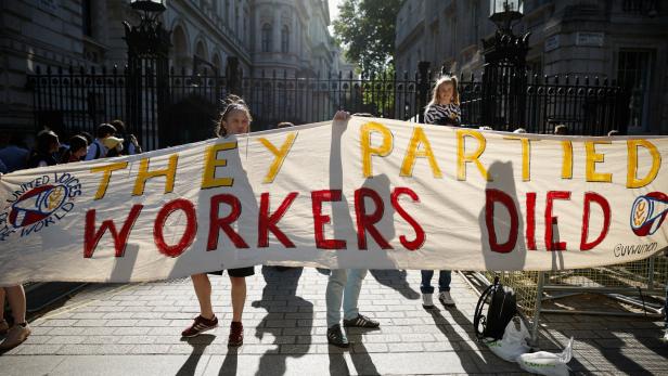 Demonstranten in London halten ein Plakat mit der Aufschrift "They partied, workers died"