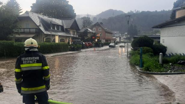 Zwei Feuerwehrleute stehen vor einer überfluteten Straße in Reifnitz.