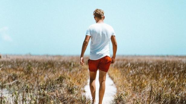 Ein Mann in Shorts geht einen sandigen Pfad entlang durch eine Graslandschaft.