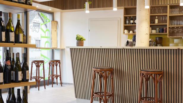 Innenansicht einer Weinbar mit Regalen voller Flaschen und Barhockern.