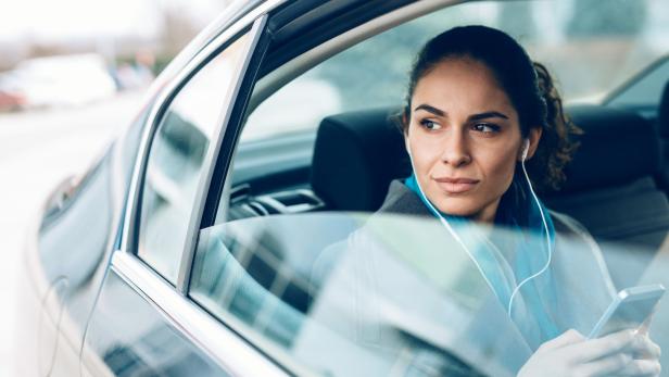 Eine Frau sitzt mit Kopfhörern im Auto und schaut aus dem Fenster.