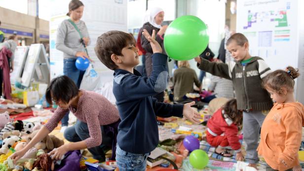 Kinder spielen mit Luftballons und Spielzeug in einem belebten Innenraum.