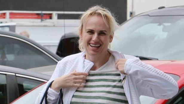 Rebel Wilson lächelt vor geparkten Autos.