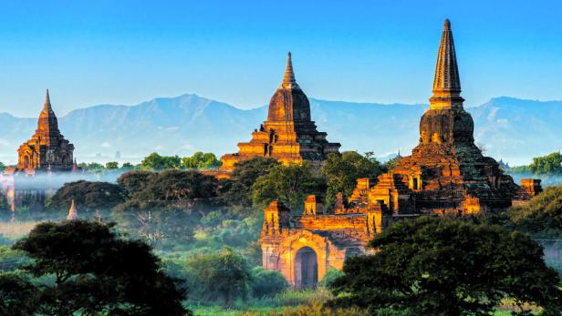 Mehrere Tempel erheben sich in Bagan, Myanmar, vor einer Bergkulisse.