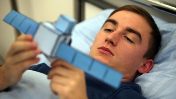 Ein Mann liegt im Bett und betrachtet ein Modell eines Satelliten.