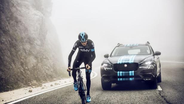 Ein Radfahrer in Team Sky-Bekleidung fährt auf einer nebligen Bergstraße, begleitet von einem Jaguar F-Pace.
