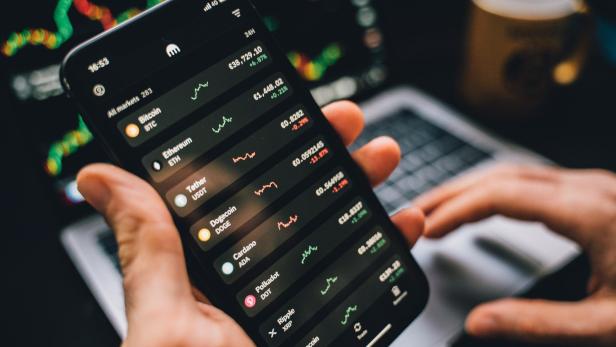 Eine Person betrachtet die Kursentwicklung verschiedener Kryptowährungen auf einem Smartphone.