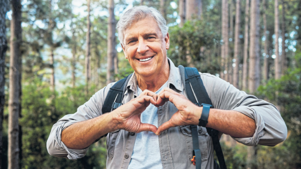 Ein lächelnder Mann formt mit seinen Händen ein Herz im Wald.