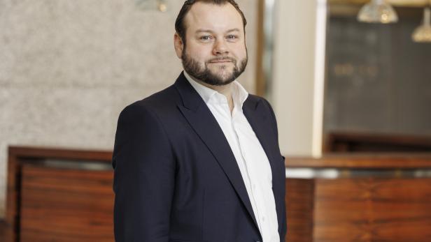 Ein Mann mit Bart trägt ein dunkles Sakko und ein weißes Hemd.