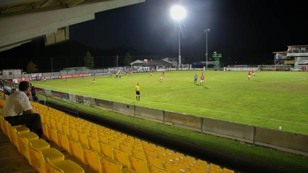 Ein Fußballspiel in einem kleinen Stadion bei Nacht.