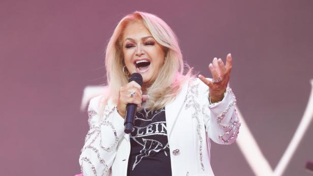 Eine blonde Sängerin mit weißem Blazer singt in ein Mikrofon.