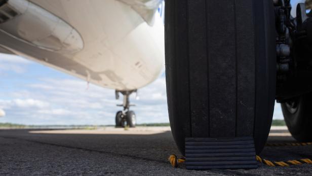 Ein Flugzeugreifen steht mit einem Unterlegkeil auf dem Rollfeld.