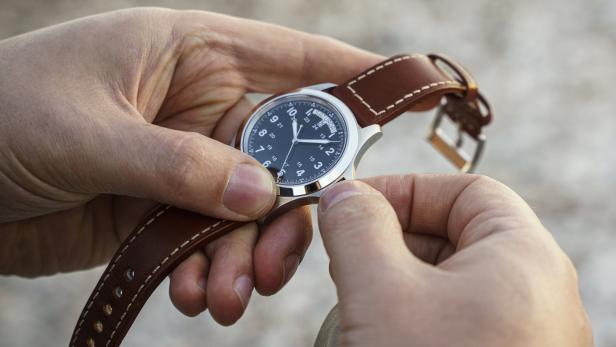 Eine Person hält eine Armbanduhr mit braunem Lederarmband in den Händen.