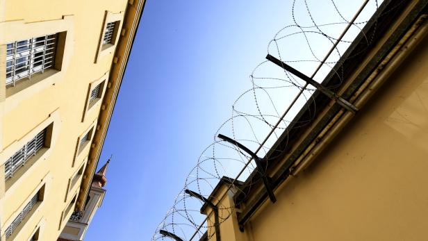 Stacheldraht auf einer gelben Mauer vor blauem Himmel.