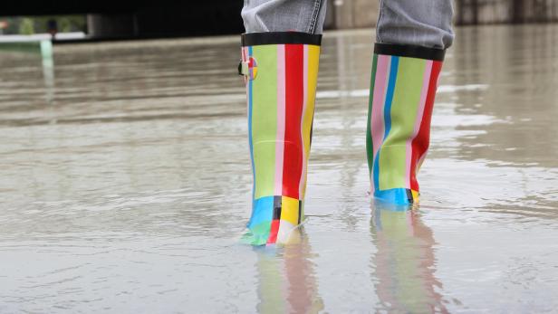 Eine Person steht mit bunten Gummistiefeln im knöcheltiefen Wasser.
